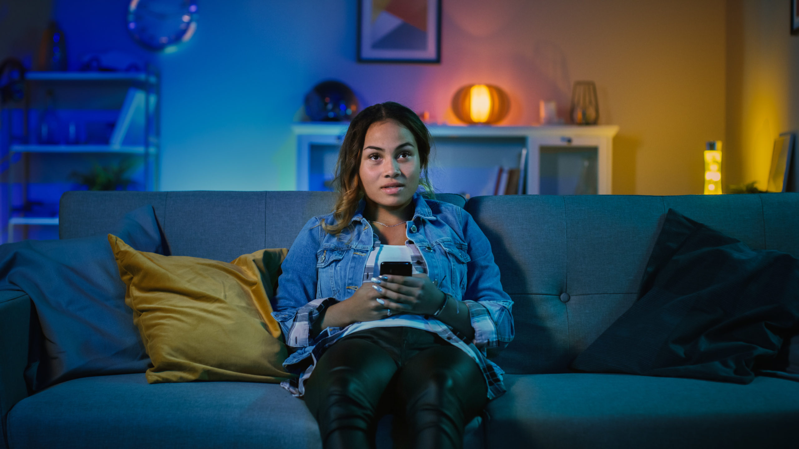 Girl sitting on a sofa holding her phone looking at TV